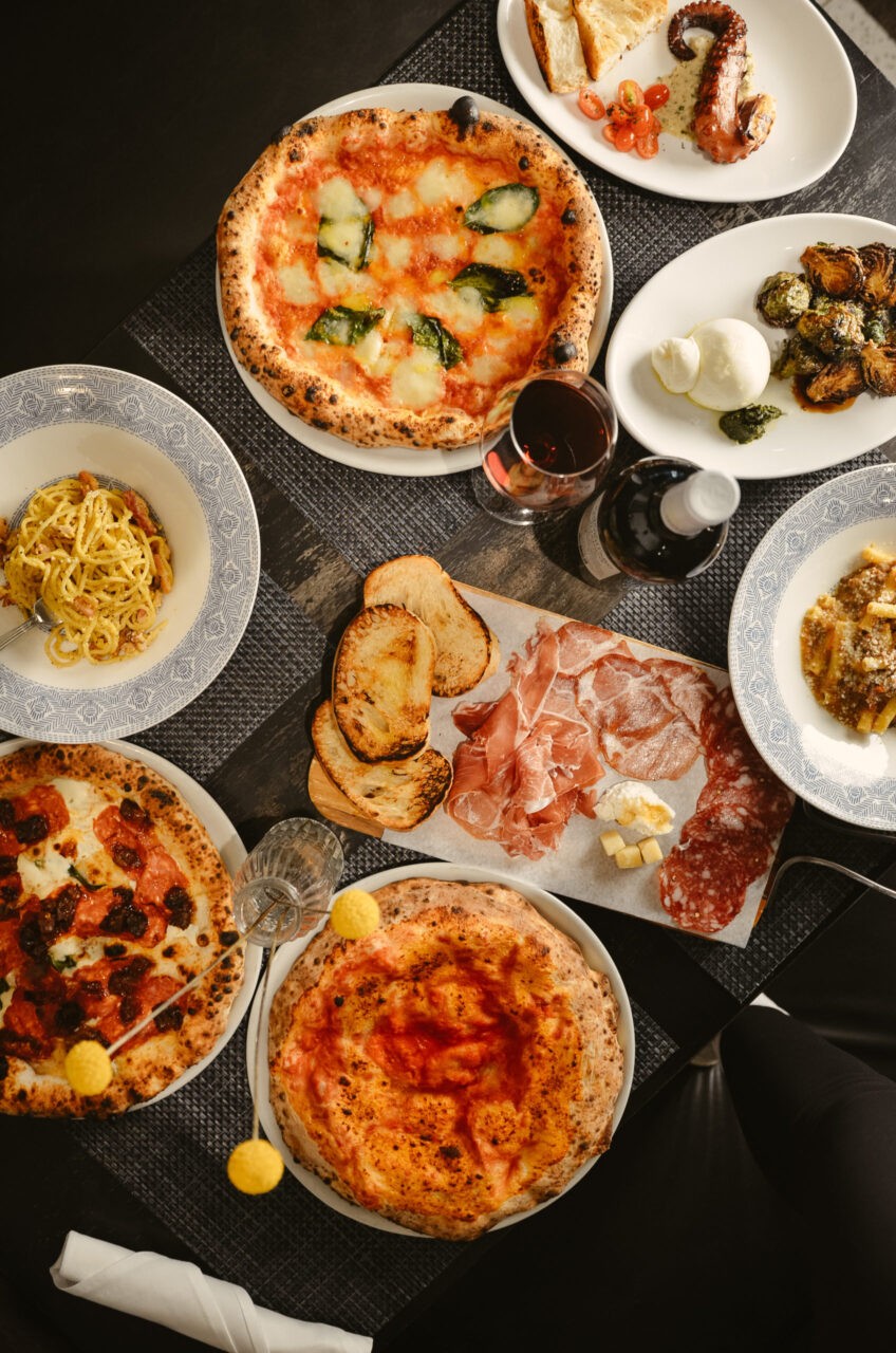 Italian dishes such as pizza, wine, breads, and pasta all displayed on a table.