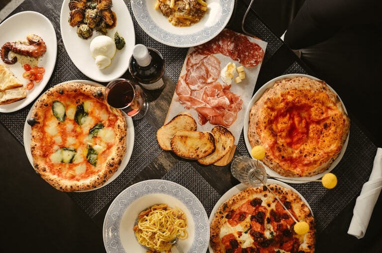 Italian dishes such as pizza, wine, breads, and pasta all displayed on a table.