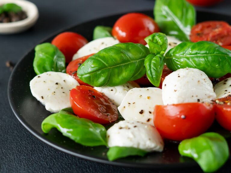Caprese salad with ripe tomatoes and mozzarella cheese with fresh basil leaves on black background. Italian food. Close-up